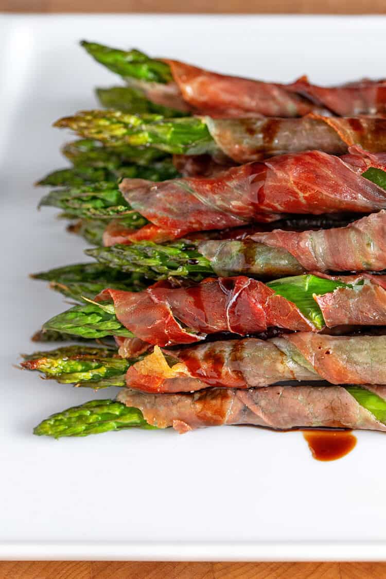 A closeup shot of broiled prosciutto-wrapped asparagus topped with aged balsamic vinegar.
