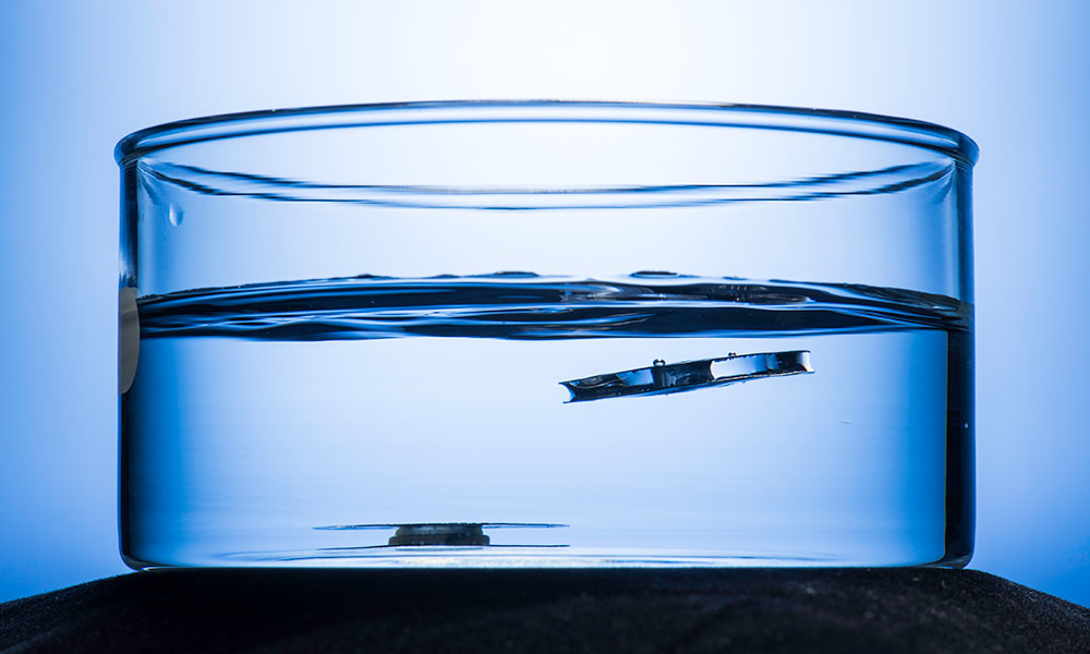 two small metal discs submerged in a tank of water, one rising to the surface