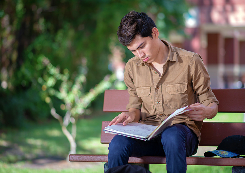 photo of male student sitting on bench outside studying