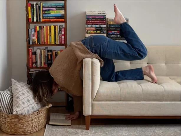 A woman leaning over a couch and reading.