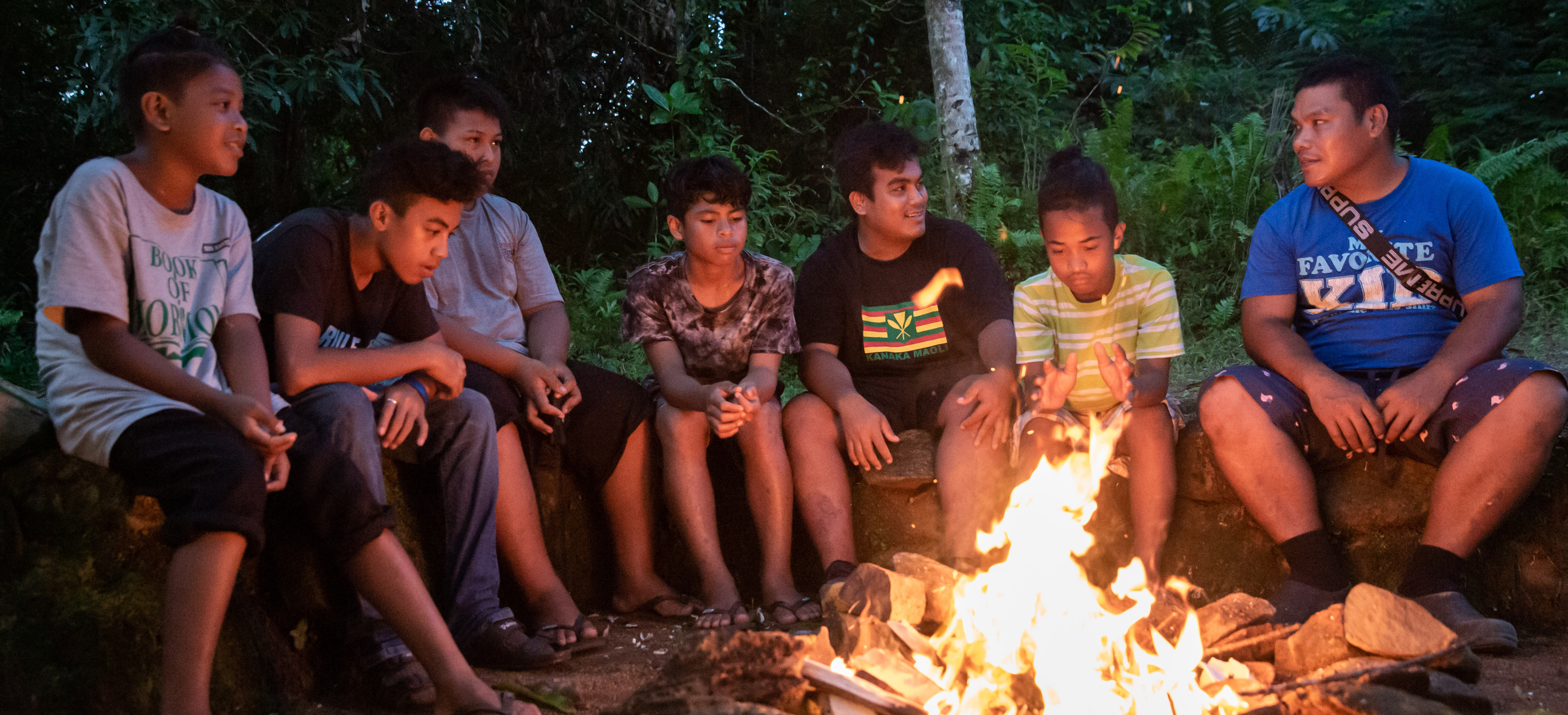 Young men and leaders sit around a campfire.