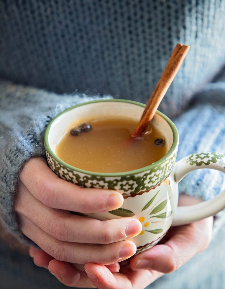 holding a mug of mulled cider with a cinnamon stick.
