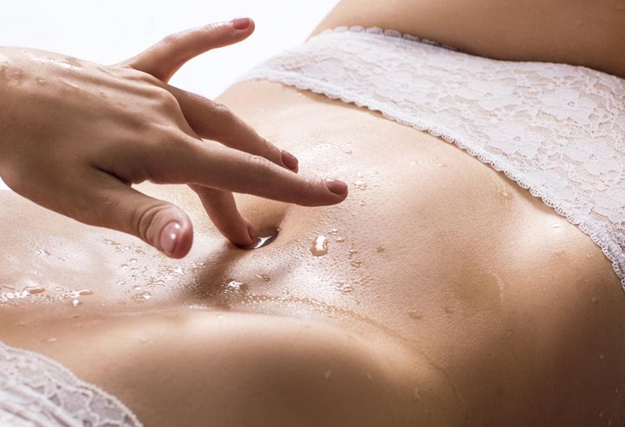 Faire squirter une femme - Main f&eacute;minine caressant le ventre d'une femme portant des sous-v&ecirc;tements, avec des gouttes de liquide sur la peau.