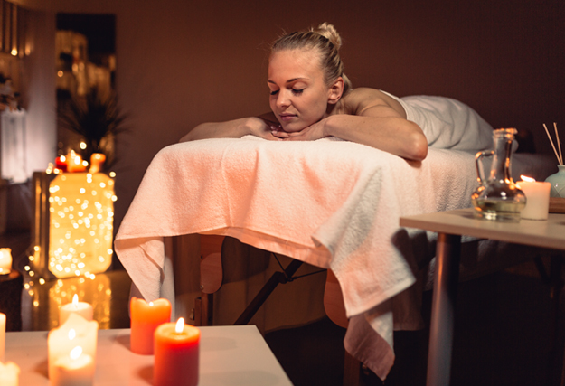 Massage tantrique pour femme - Femme se d&eacute;tendant sur une table de massage entour&eacute;e de bougies allum&eacute;es, dans une ambiance tamis&eacute;e.