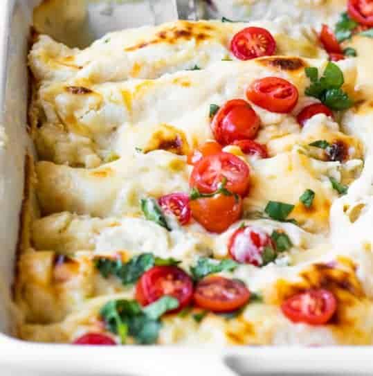 Baking dish filled with cheese breakfast enchiladas topped with diced tomatoes and cilantro.
