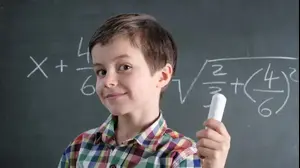 ילד עם גיר ביד מחייך ליד לוח עם נוסחאות מתמטיות