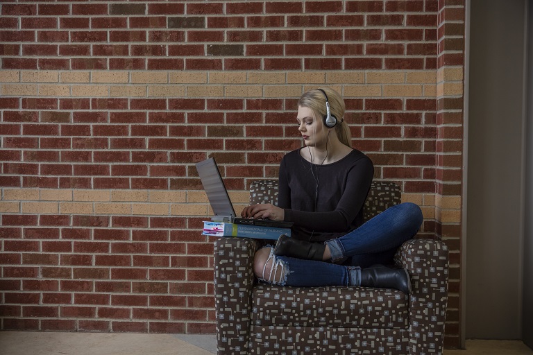 female student sitting in chair wearing headphones working on a laptop