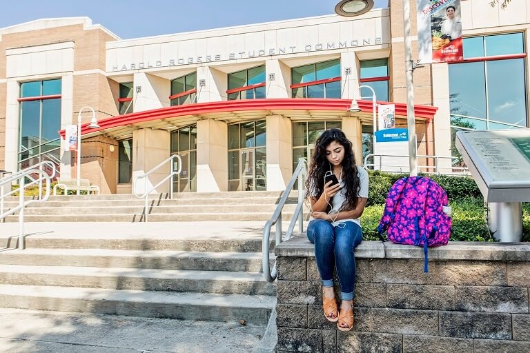 female student playing on cell phone outside of classroom building