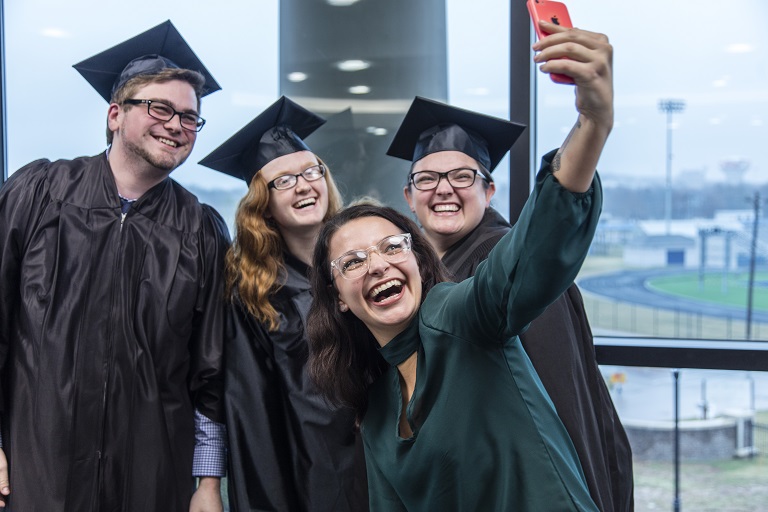 four students at graduation taking a selfie