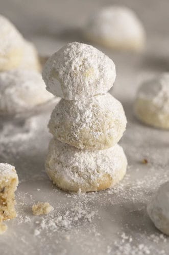 Three Russian tea cakes stacked on a marble table sprinkled with powdered sugar