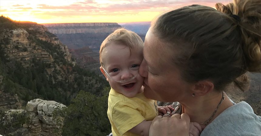 Mother kissing her baby with oxygen tubs in his nose in the mountains during sunset
