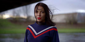 Portrait close-up dark-haired young smiling pretty girl walking on the street by the river under the bridge, she has bright makeup and red lipstick, nose and lip piercing.