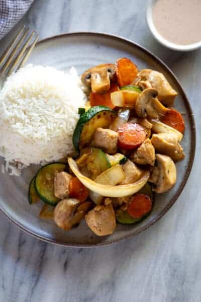 Hibachi chicken stir-fry with a side of rice and yum yum sauce in the background.