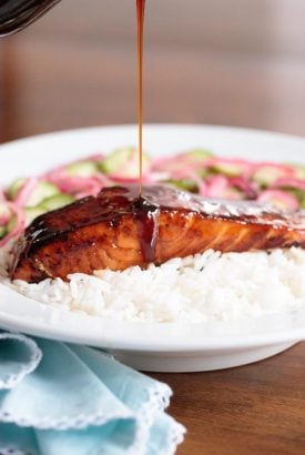 Vertical picture of honey coriander salmon with rice and sauce drizzled over the top in a white bowl