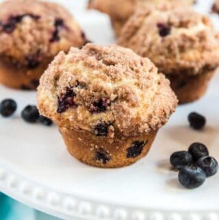 bluberry muffin with streusel topping on white plattter with blueberries