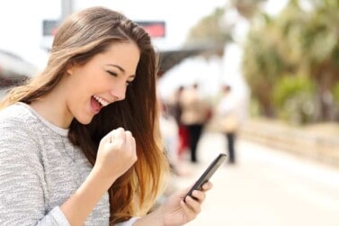 young woman outside with phone in hand happily making a fist and smiling at phone