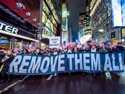 Protesters hold a banner reading "REMOVE THEM ALL" while marching en masse down the middle of a city street