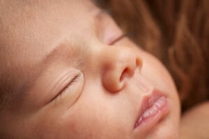 Close-up photo of a sleeping baby with eyes shut, showing a peaceful expression. The image highlights the baby's delicate skin, closed eyes, small nose, and slightly parted lips. As you search for baby names 2024, let this serene moment inspire your choice. The background is softly blurred.