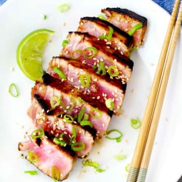 A plate with seared ahi tuna steak, chopsticks, a lime wedge, and scallions.