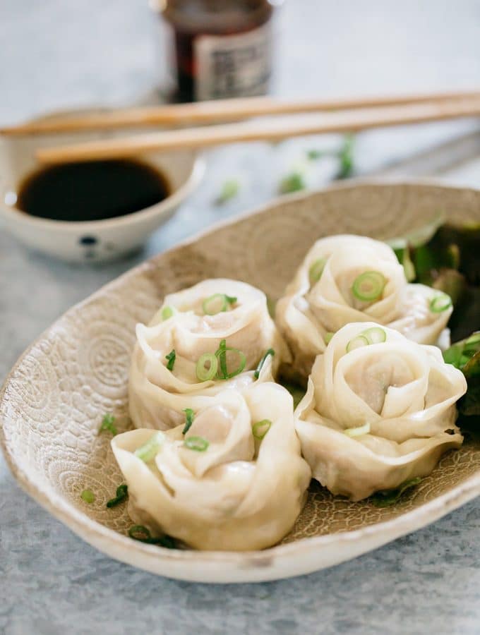 four rose dumplings served on a oval plate with a small bowl of dippping sauce and a pair of chopstick