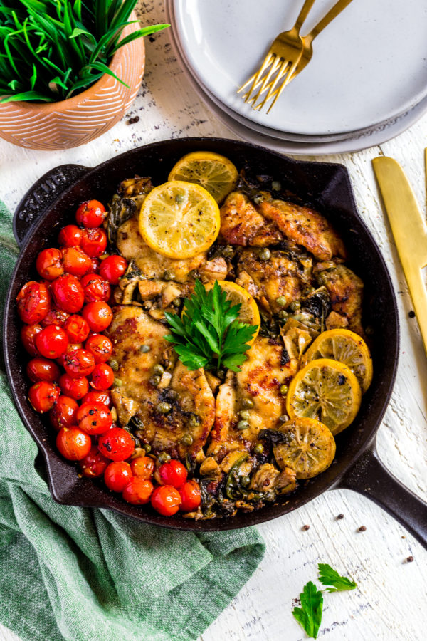 Healthy Chicken Piccata with lemon, tomatoes, artichokes and spinach served in a cast-iron skillet.