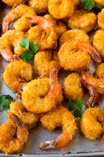 A pile of crispy coconut shrimp on a sheet pan with cilantro leaves for garnish.