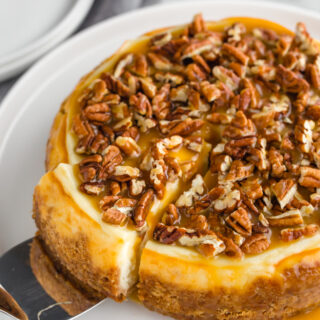 A whole instant pot cheesecake topped with caramel and pecans, with a slice cut and partially pulled out.