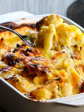 Cheesy Cauliflower Casserole being scooped from the pan with strings of cheese hanging from the spoon