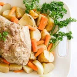 Crock Pot Pork Roast on a white tray with vegetables and a spray of parsley on the side