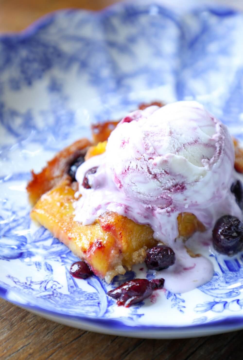 Keto Peach and Blueberry Slab Pie on a blue and white plate with a scoop of mixed berry ice cream on top