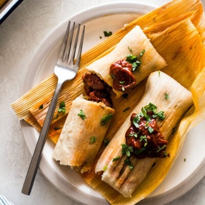 Pork Tamales with red chile sauce on corn husks.