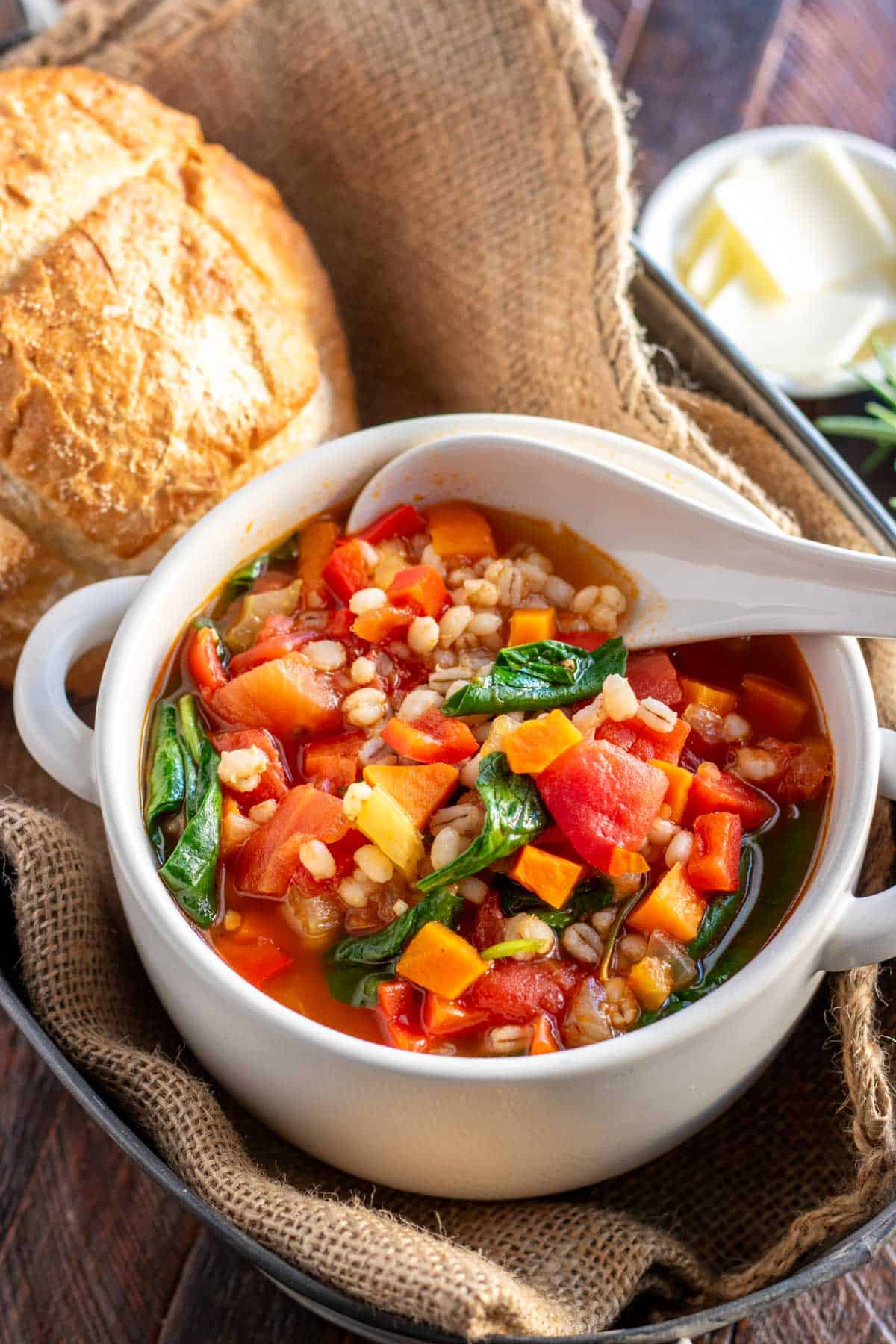 vegetable barley soup in a white bowl with a bread roll