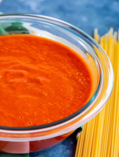 Bowl of San Marzano Tomato Sauce next to pile of uncooked spaghetti noodles