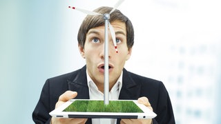 Ein Mann h&auml;lt einen Tablet-Computer in den H&auml;nden, aus dem ein Windrad zu wachsen scheint.